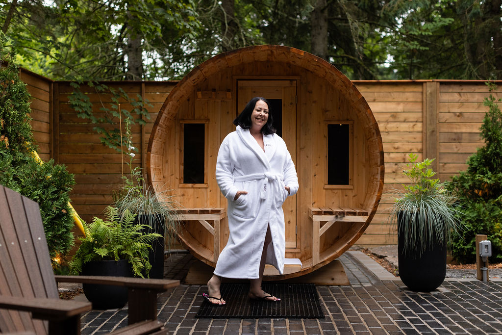woman in a white bath robe posing in front of a Finnish barrel sauna at Liberty Inn in Caledon ontario
